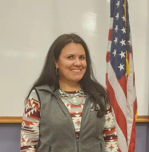 Woman in a patterned top stands beside an American flag.