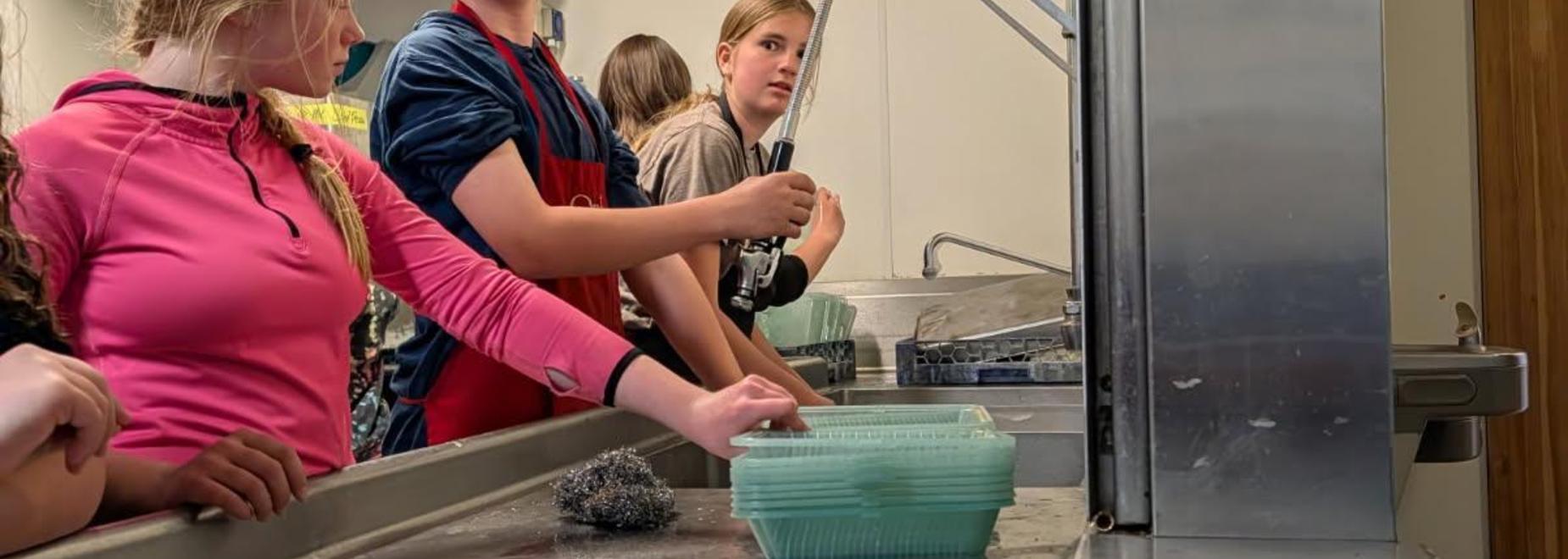 Kids washing dishes together in a kitchen setting.