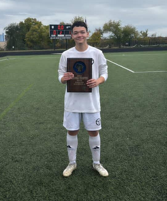 Gio standing in his soccer uniform holding the regional champions plaque.