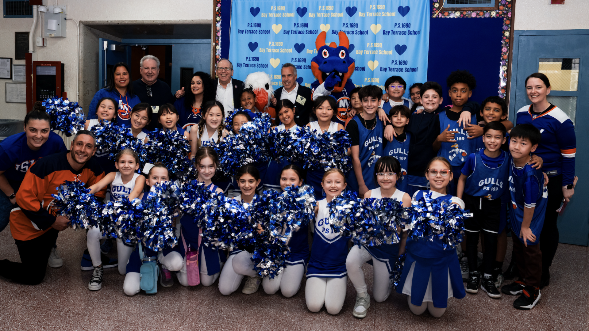 A large group of children in cheerleading outfits posing with adults and a mascot.