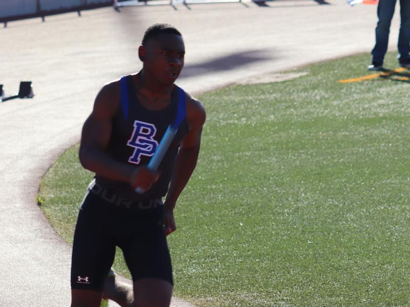 A runner in athletic gear sprinting on a track, holding a relay baton.