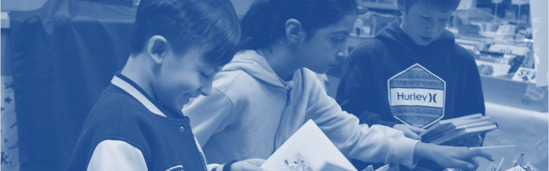Two boys and a girl look enthusiastically at a table of books