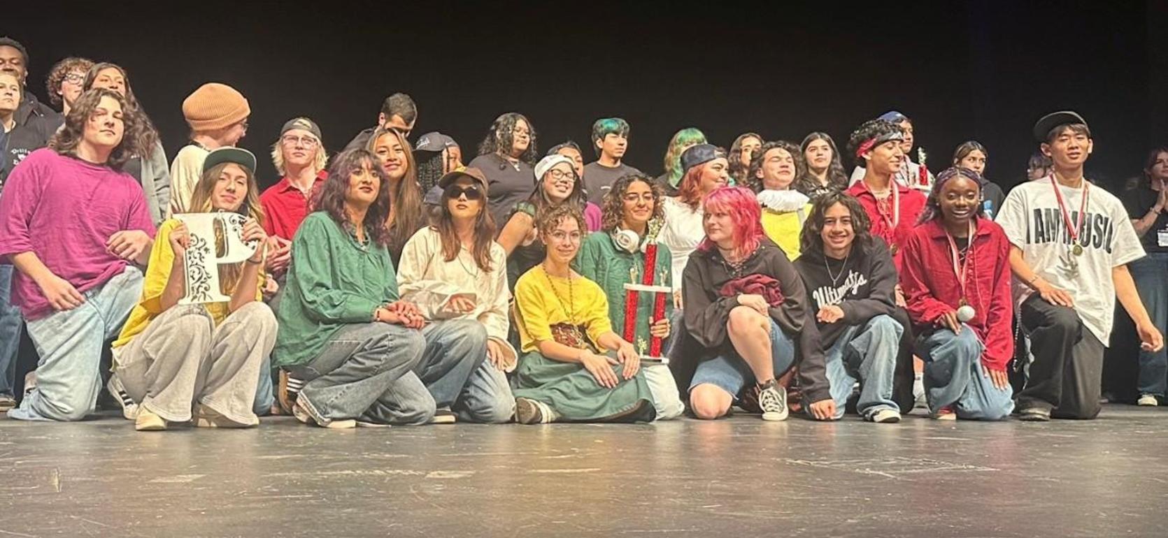 Large group of students celebrating on stage with awards and colorful outfits.