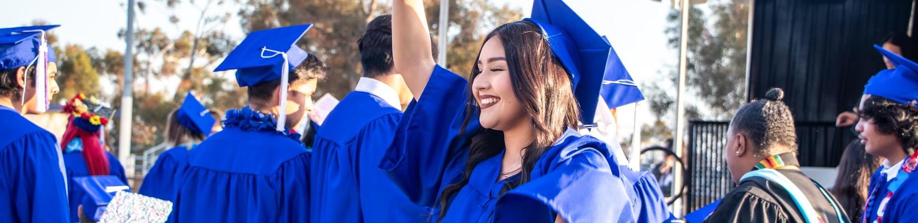 A woman in a blue graduation gown proudly holds her diploma, celebrating her academic achievement with a joyful expression.