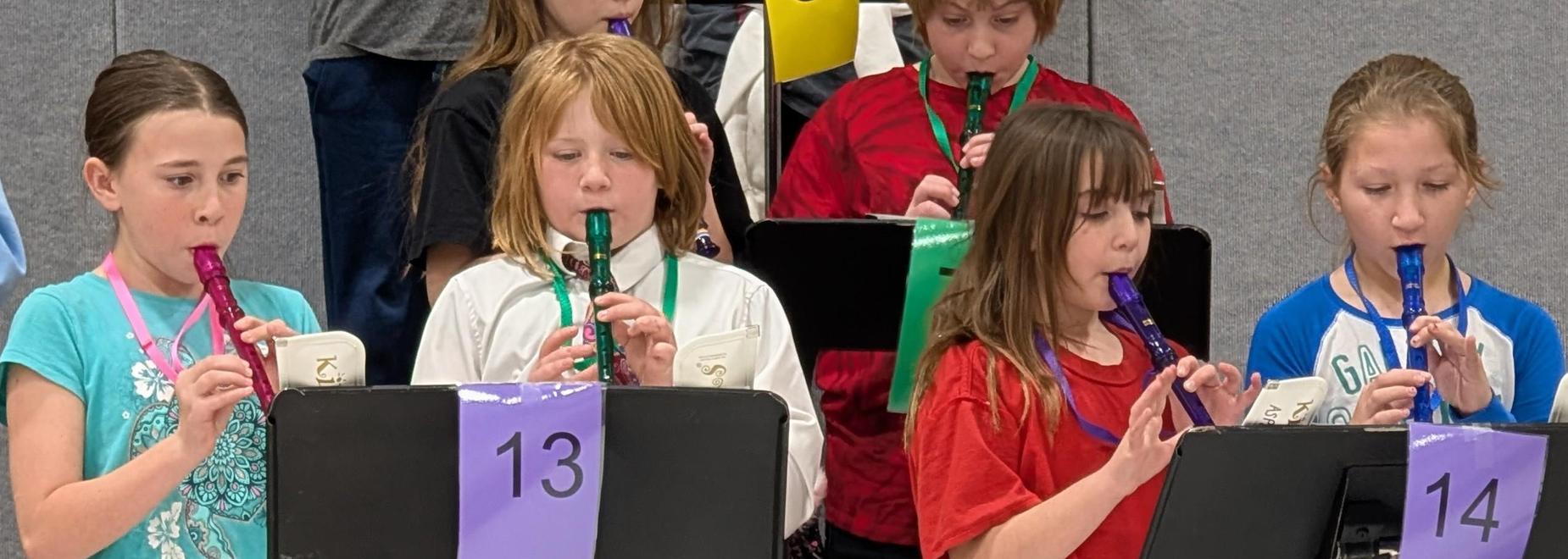 Four children playing recorders in a music class with sheet music.