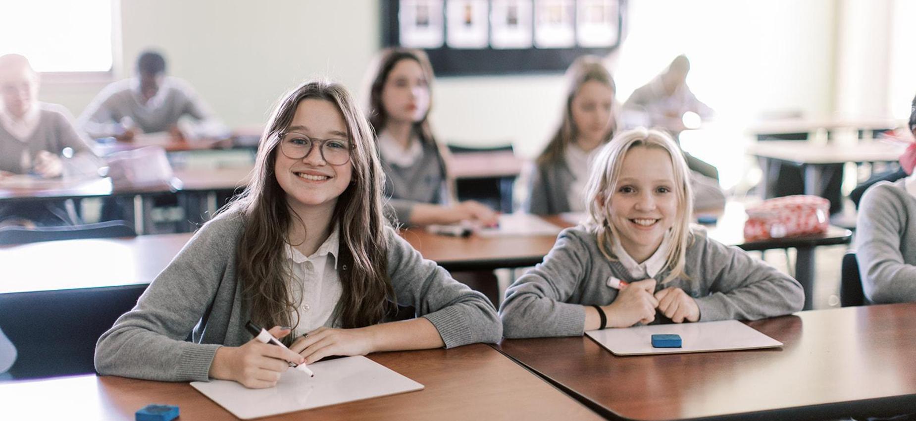 Two smiling students at their desks during class at Founders Classical Academy of Tyler