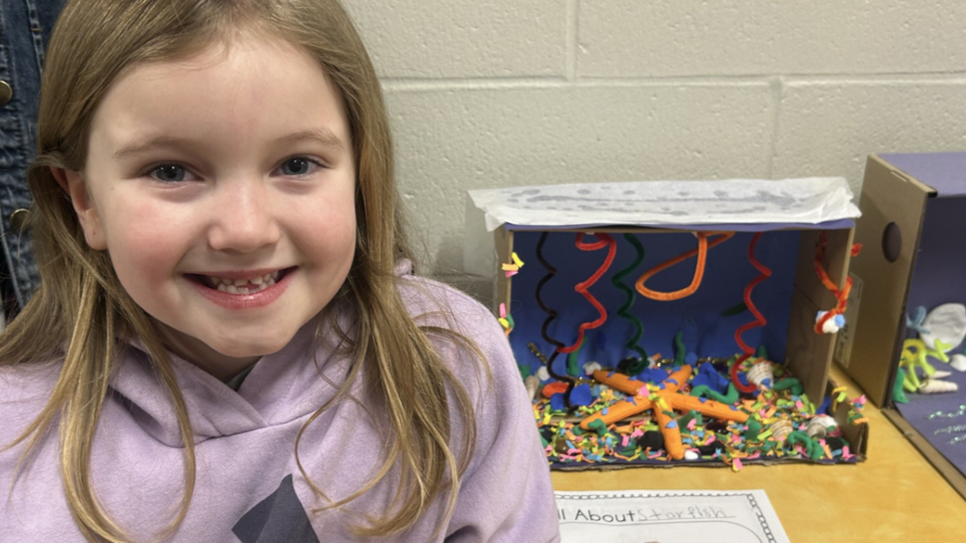Girl smiling beside a colorful craft project with decorations and a paper star.