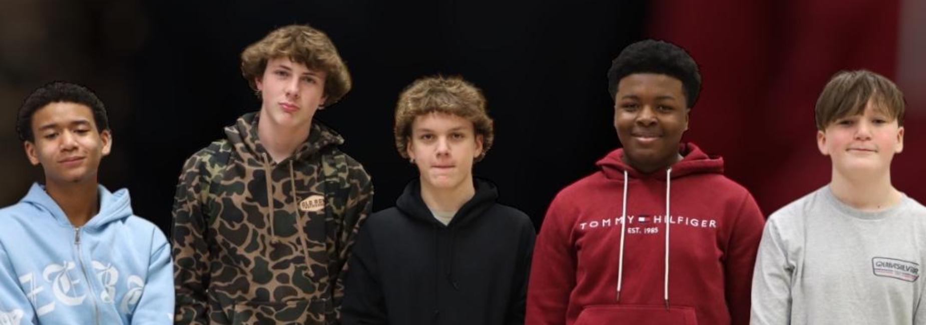 Five teenage boys stand together smiling in casual hoodies.