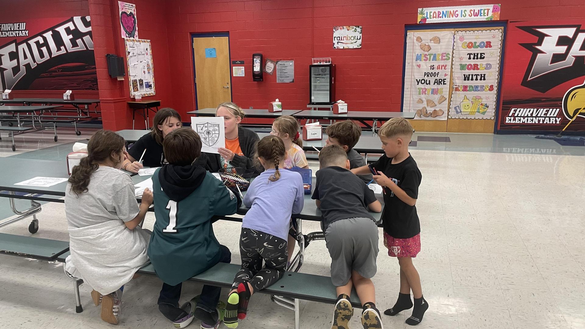 Children and adults engaged in a group activity at a cafeteria table.