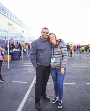 A couple posing outdoors at an event, with tents in the background.