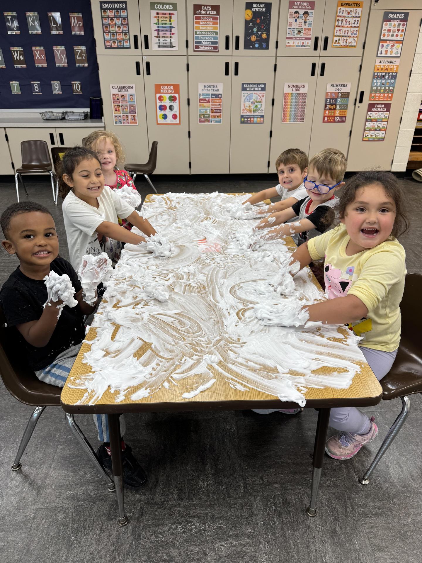 Six students at a table doing a sensory activity with white shaving foam on a table
