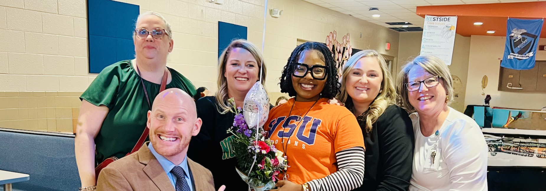 Group of six people celebrating with flowers and smiles.