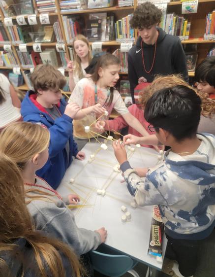 Students collaboratively building a structure with marshmallows and spaghetti.