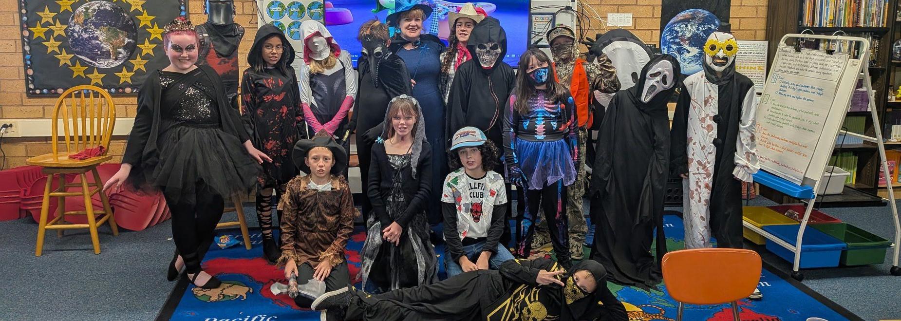 A group of children in costume for a Halloween-themed event, posing together in a classroom.