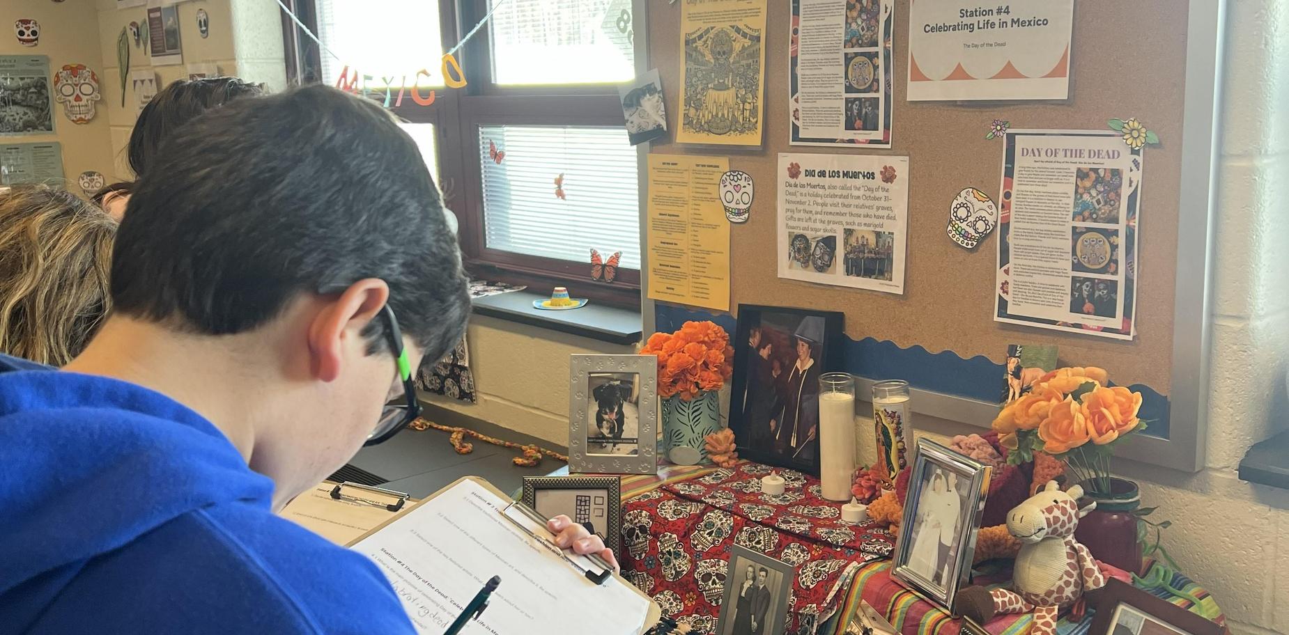 Students examine an altar dedicated to D&iacute;a de los Muertos with decorative items.