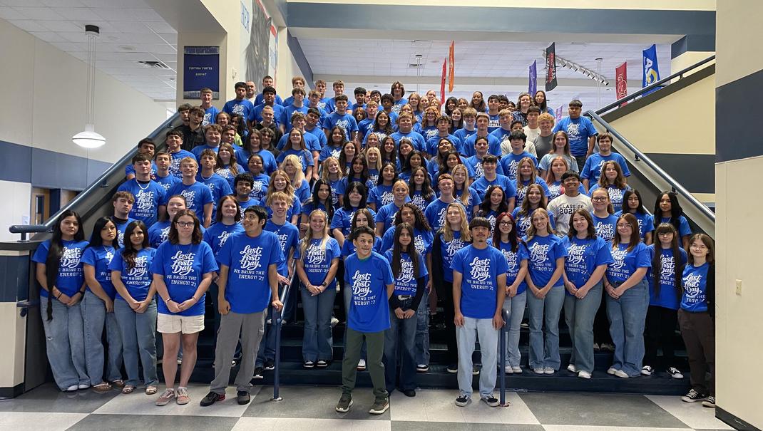 A large group of students and staff in matching blue shirts on stairs.