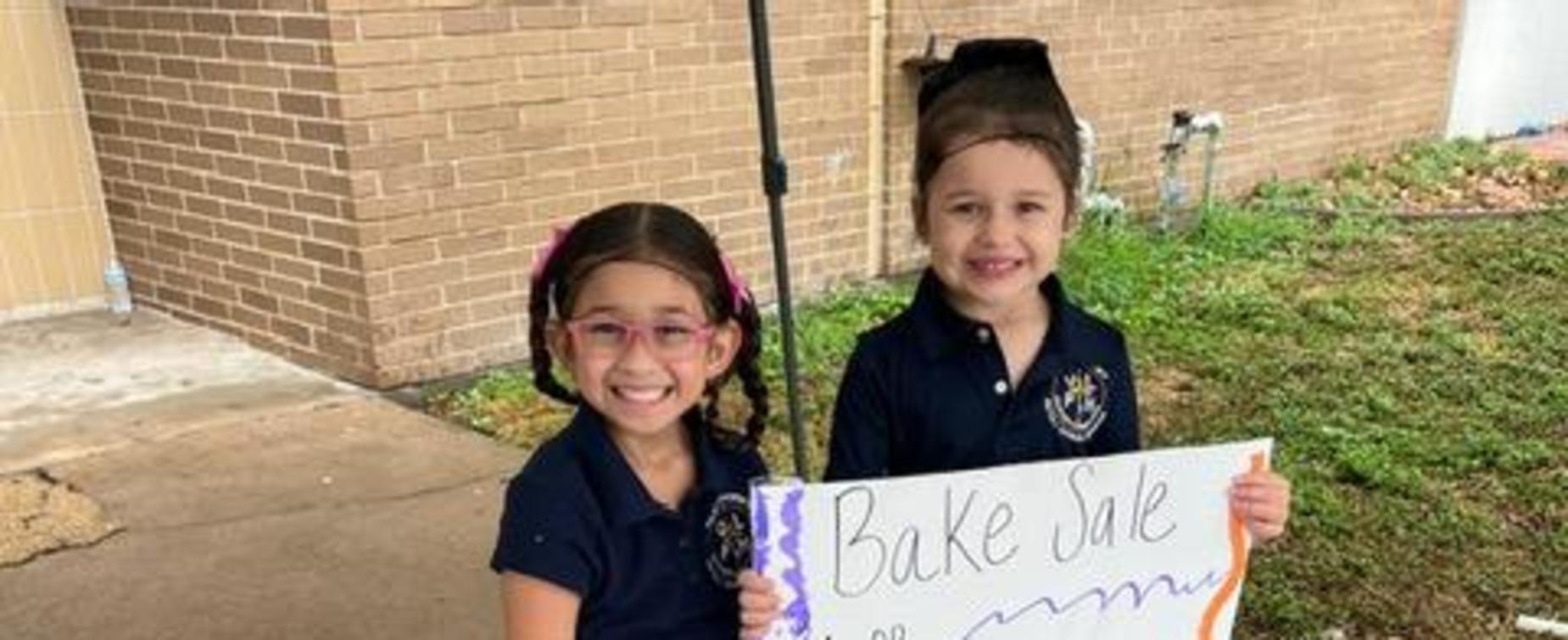 Two children holding a sign for a bake sale.