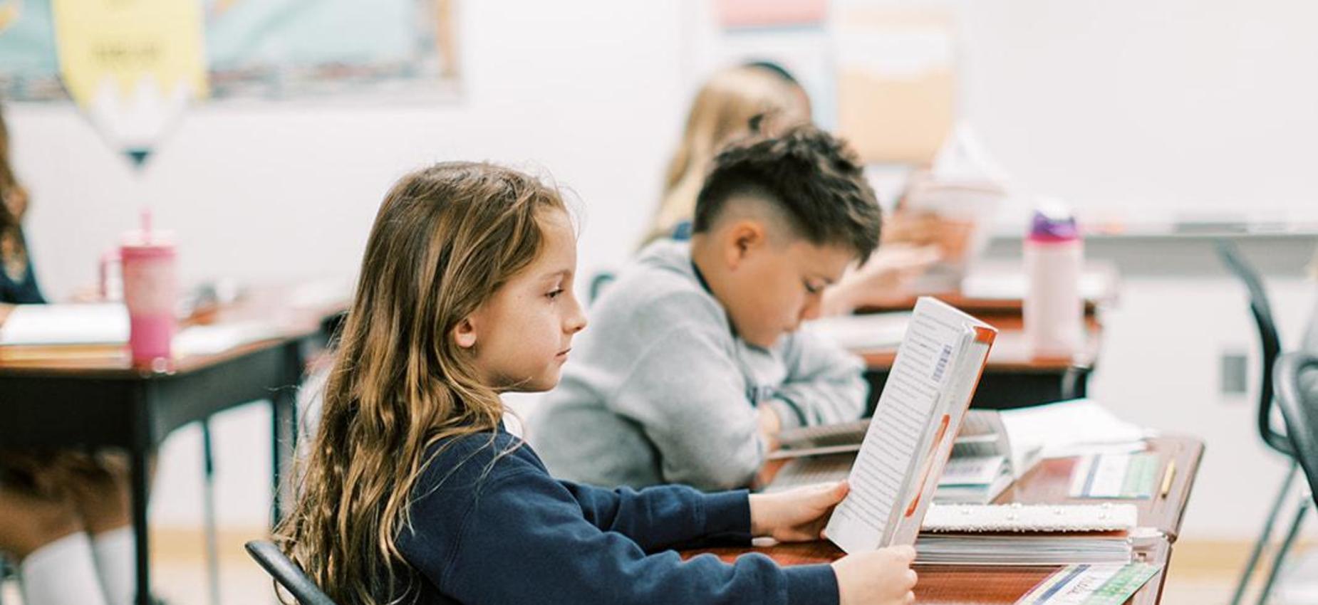 Elementary students work at their desks in a sunny classroom