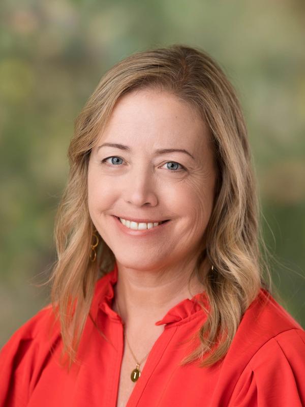 Smiling woman with long blonde hair wearing a red blouse and gold earrings.