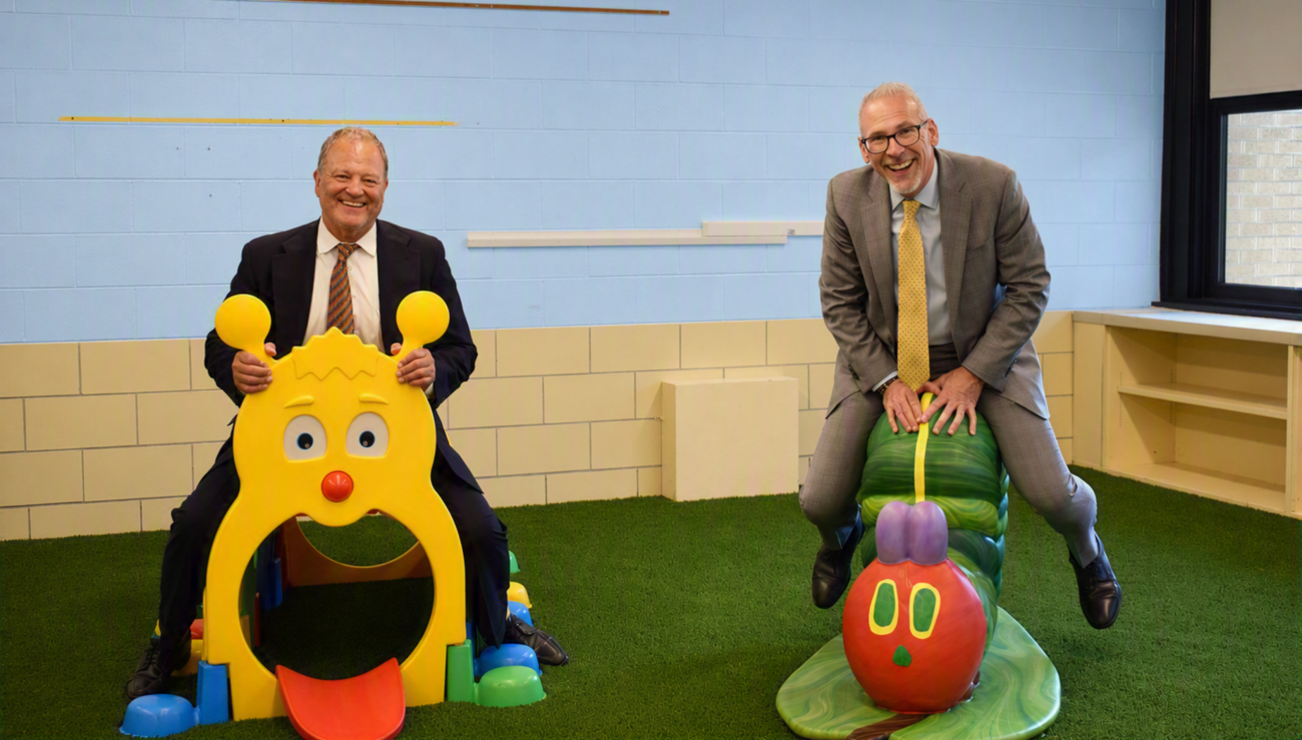 Two men playfully pose on colorful playground equipment.