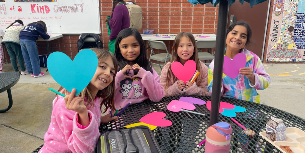 Girls showing colorful heart shapes at an arts and crafts table.