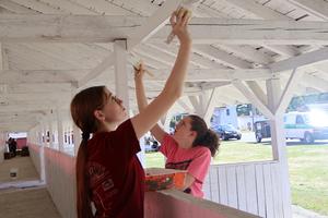 Two students paint a white beam in a livestock barn