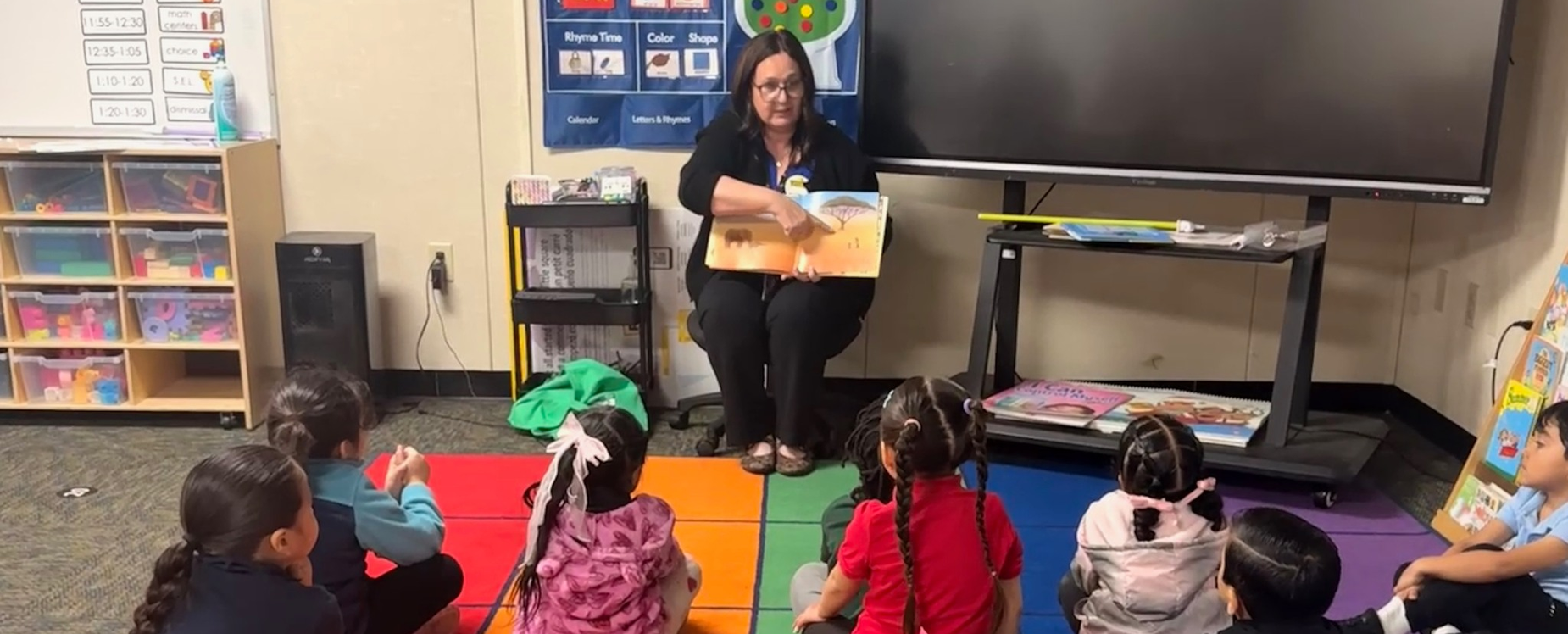 young students listening to their teacher reading from a book