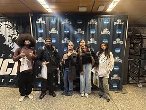 A group of five people posing in front of a school banner.