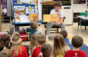 A middle school student reading to a group of kindergarteners.