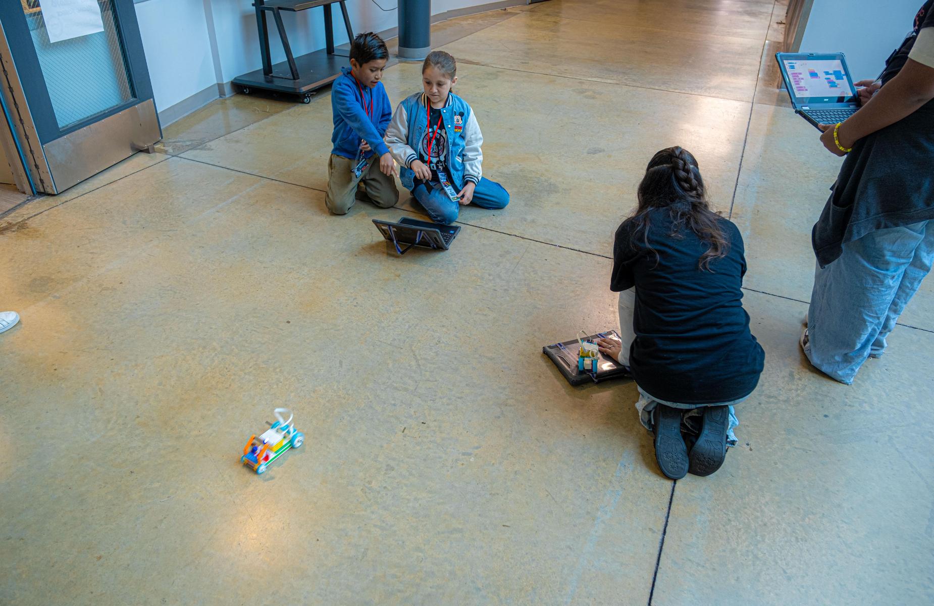 four persons engaged coding their robots on the floor of a school