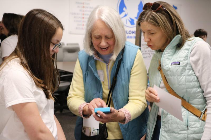 a teenage girl and two older women look at game console, ssmiling