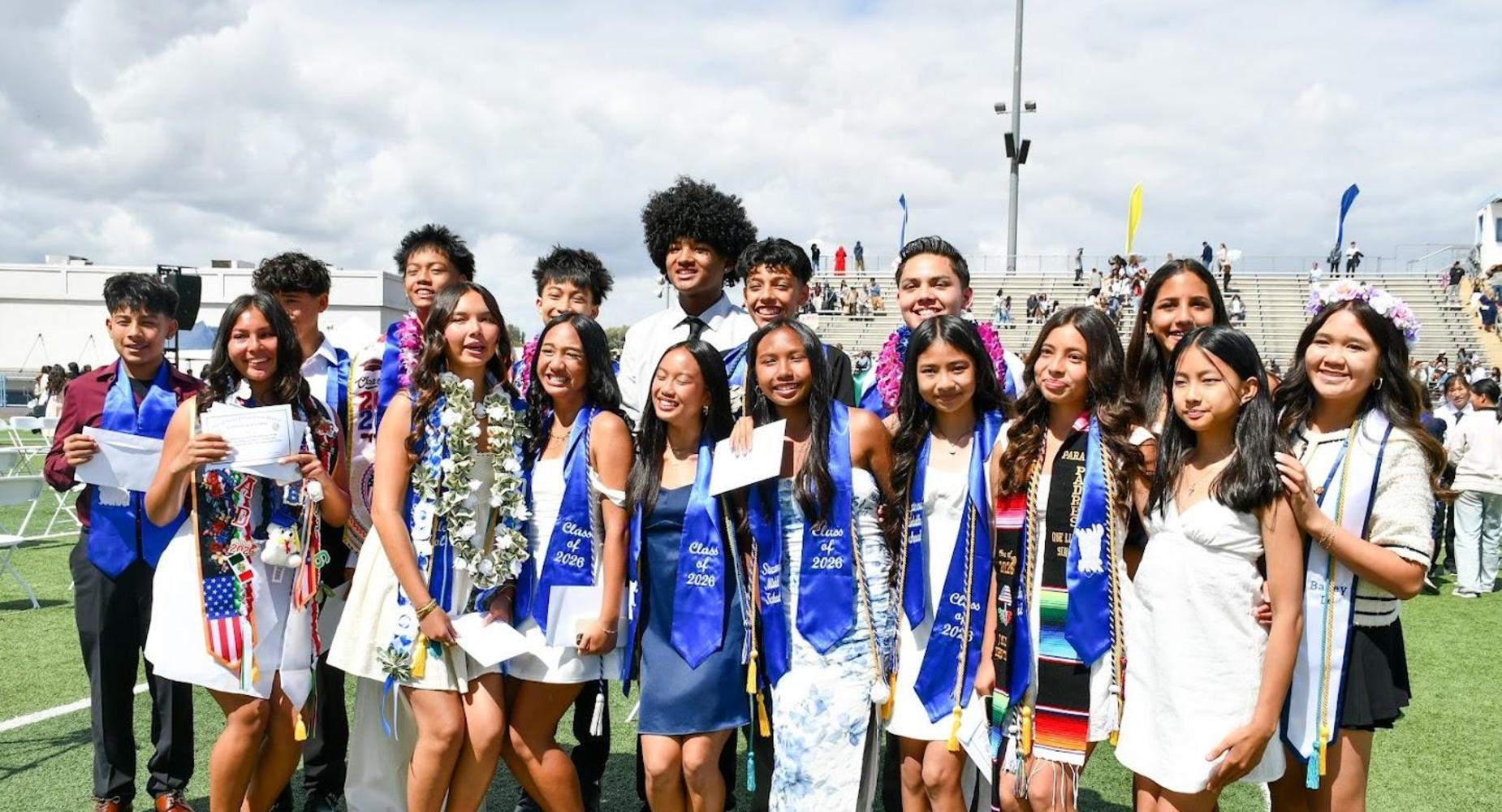 Group of graduates cheerfully posing at a ceremony outdoors.