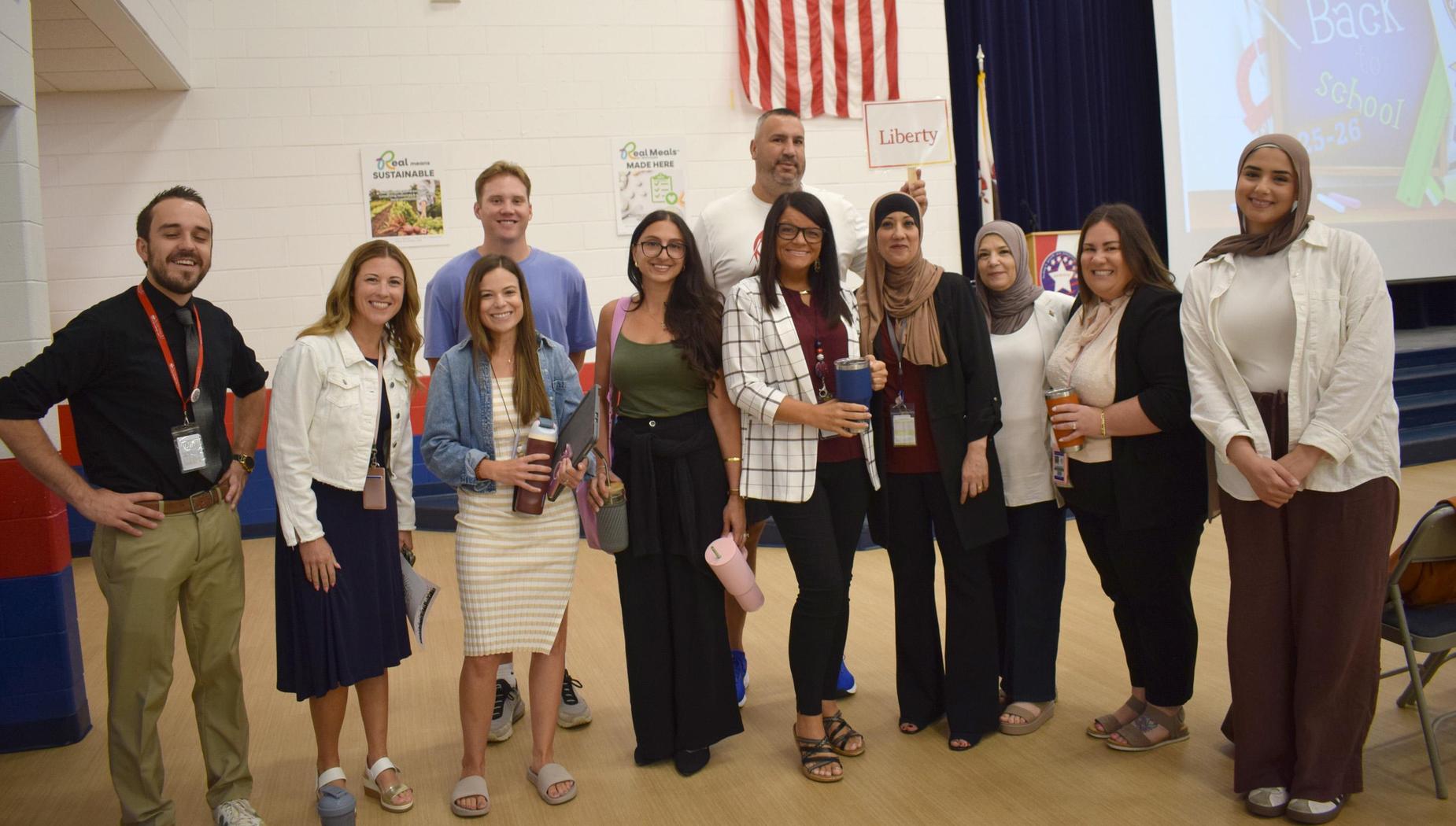 Group of ten educators posing together in an auditorium with a projector screen behind them.