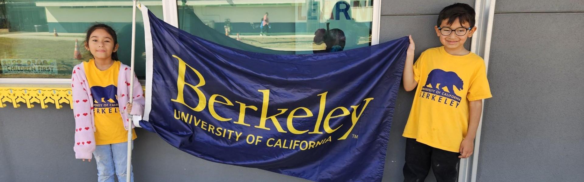 Two children holding a University of California, Berkeley flag outdoors.