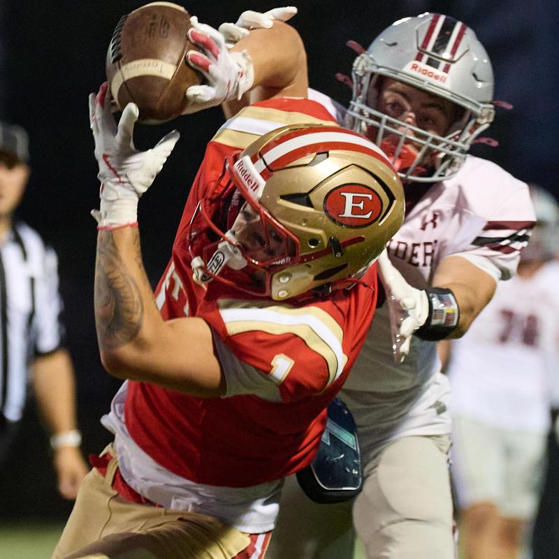 Football player in a red jersey catching the ball while being tackled.