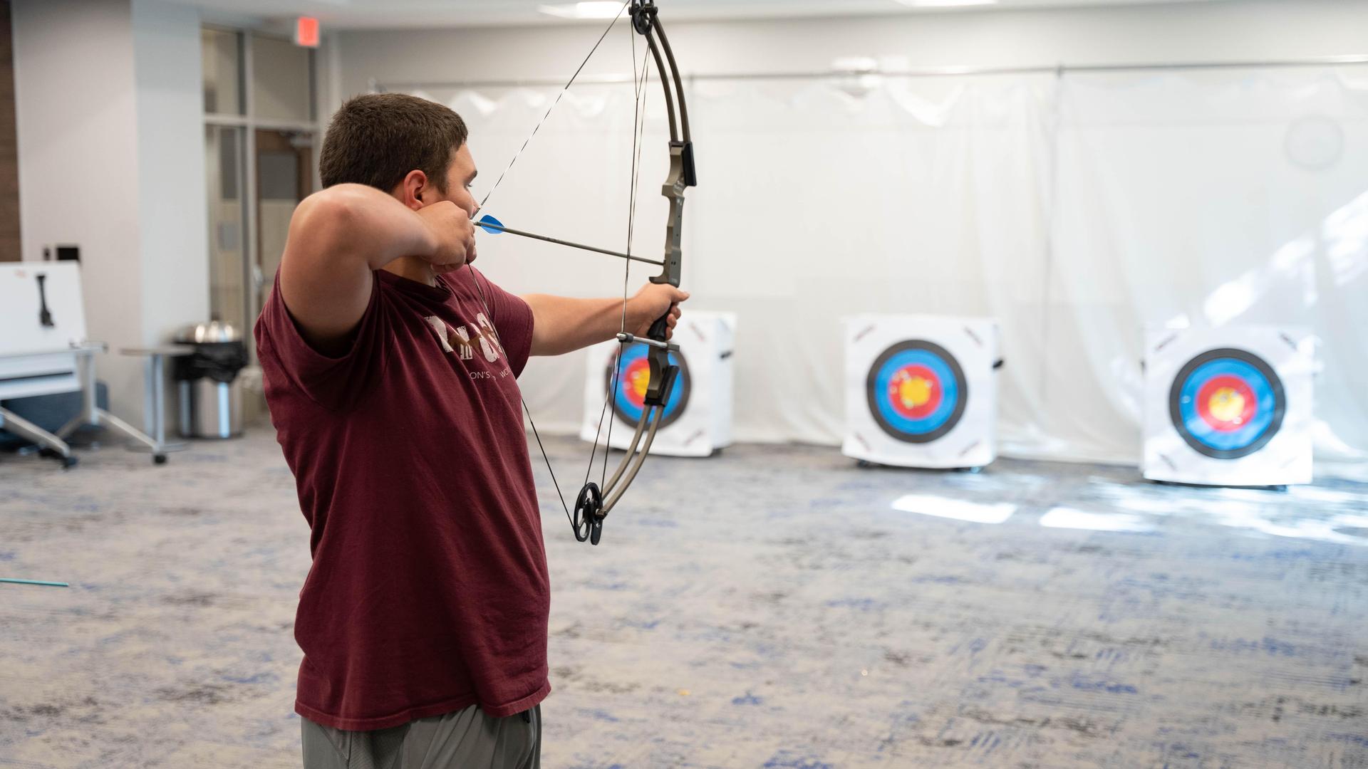A person aiming an arrow at targets in an indoor archery range.