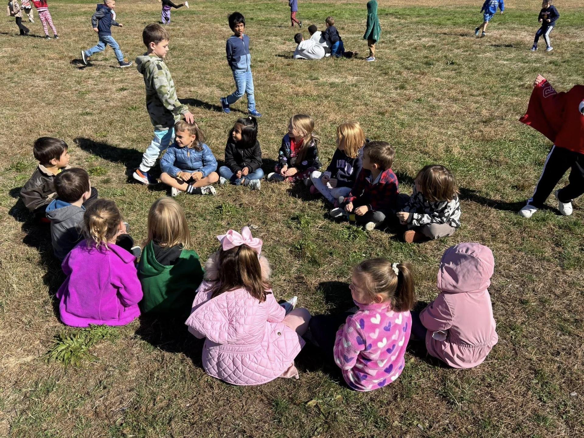 students sitting in a circle playing duck duck goose at recess