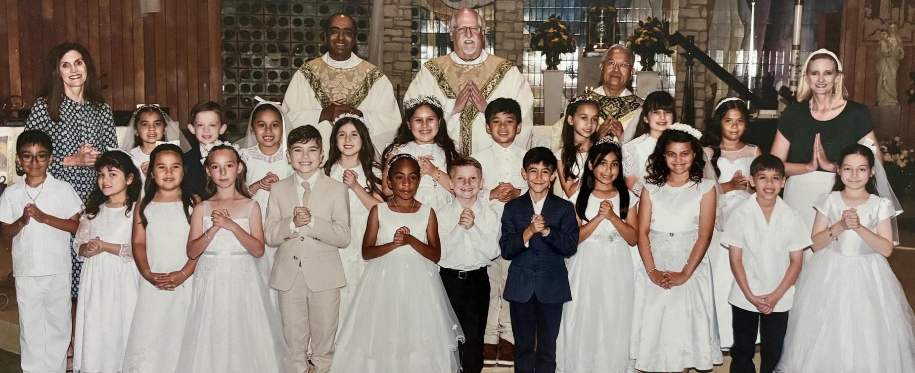 Group of children in white dresses with adults in religious attire, smiling together.