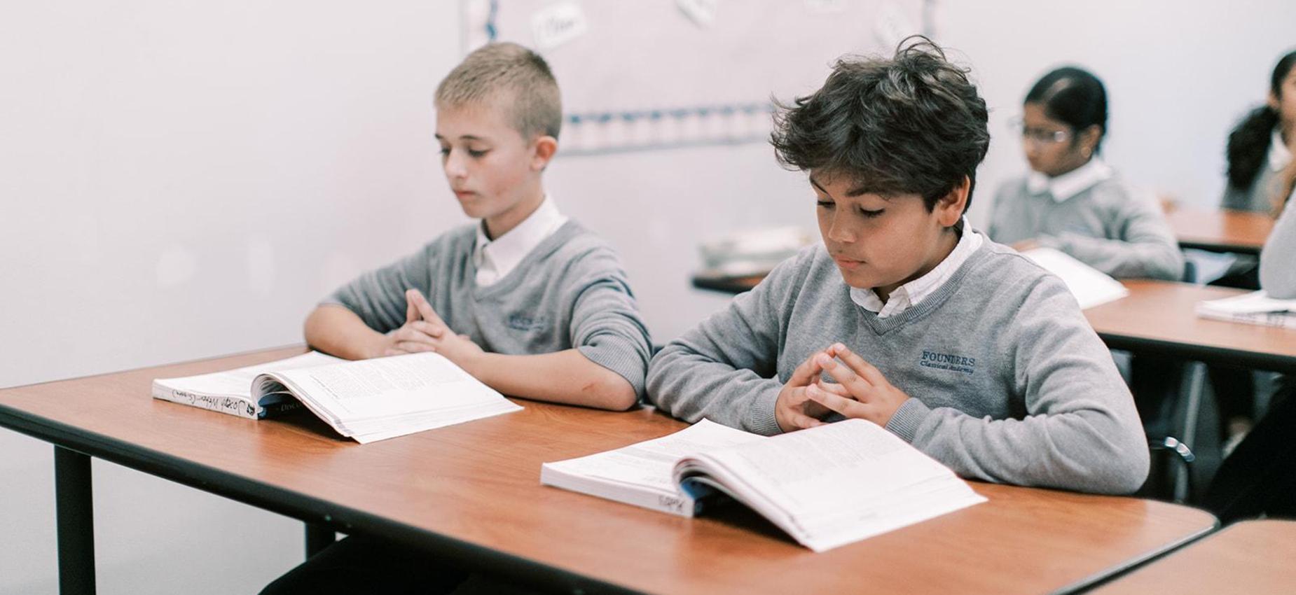 Two students read at their desks during class