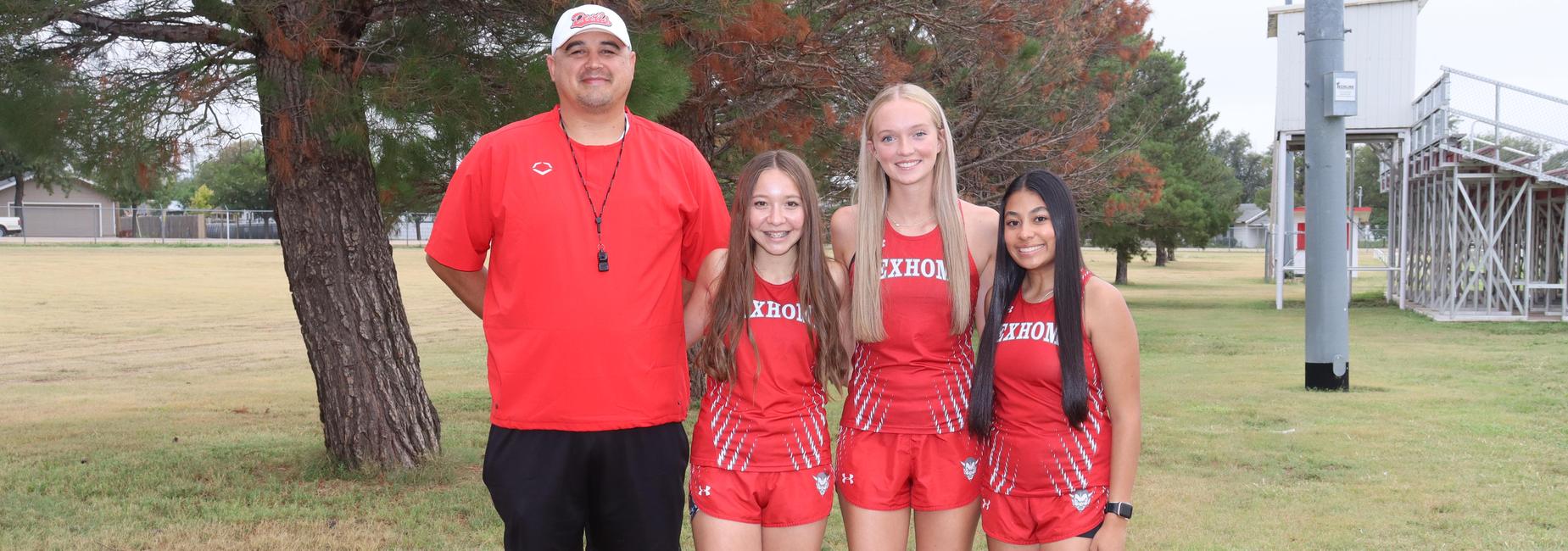 Coach and three female athletes in red uniforms smiling on a grassy field.