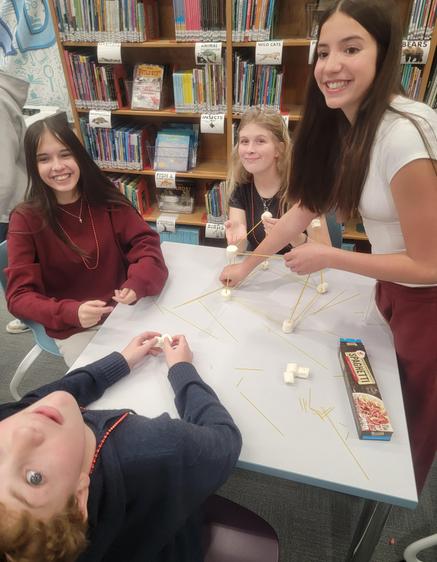 Participants smiling while constructing a project with marshmallows and spaghetti.