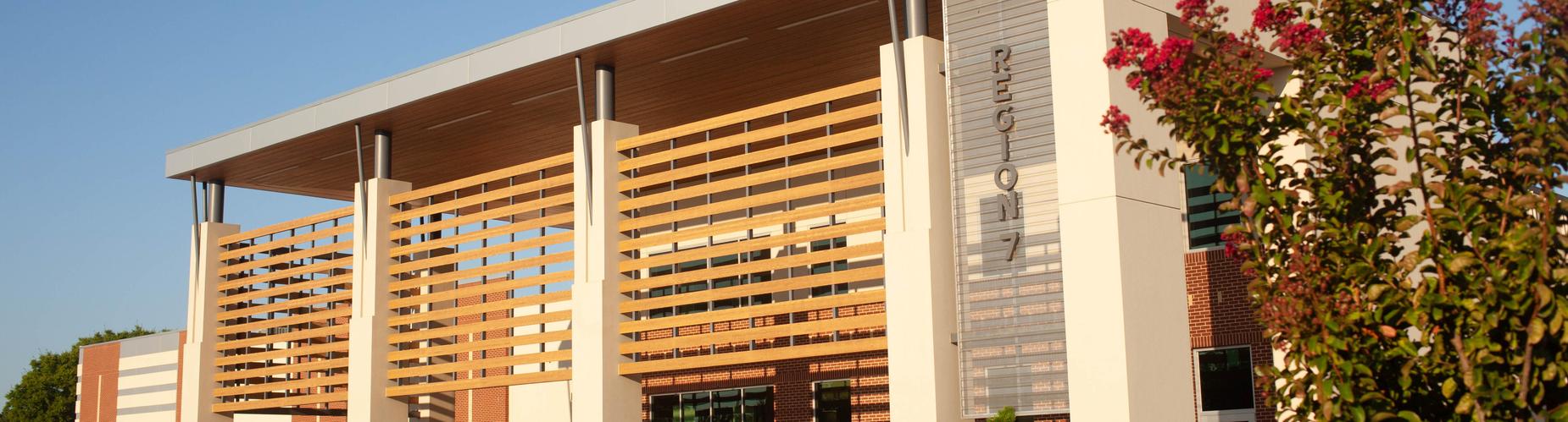 Modern building with wooden slats and colorful landscaping under a clear blue sky.