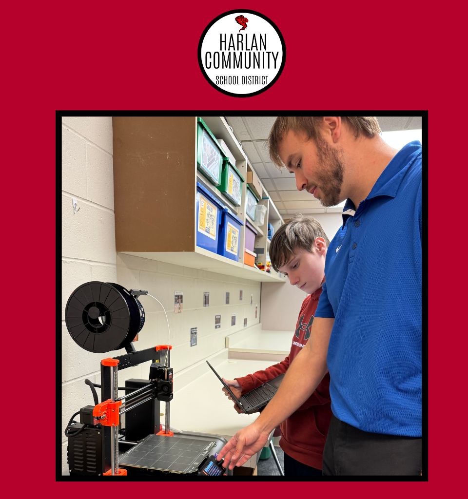 A teacher and a student work together on a 3D printer in a classroom.