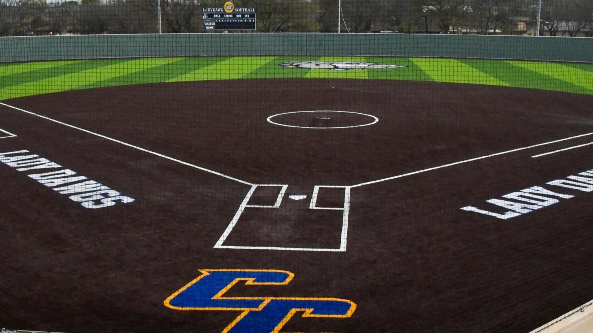 A softball field with dark brown and green grass marked for play with logos.