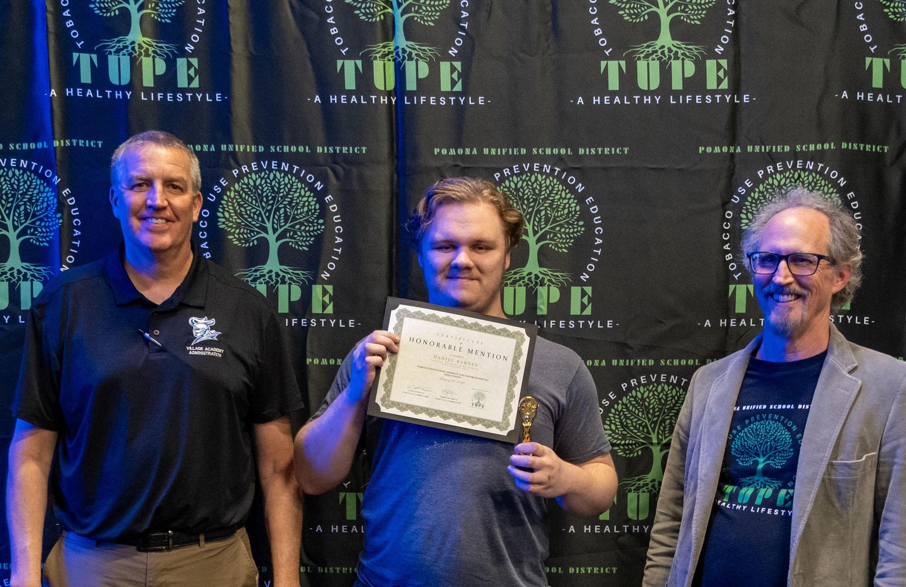 3 persons one holding a trophy and certificate