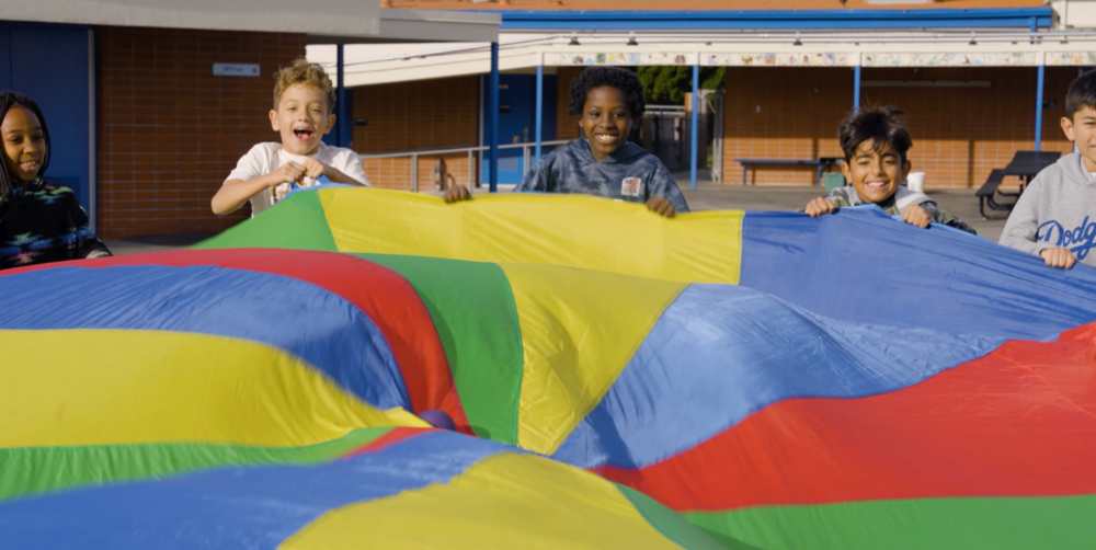 Children joyfully lifting a colorful parachute together outdoors.