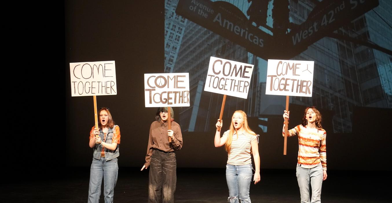 TKHS students hold signs that say, "Come Together" in one scene of the fall play "A Trip to the Moon."