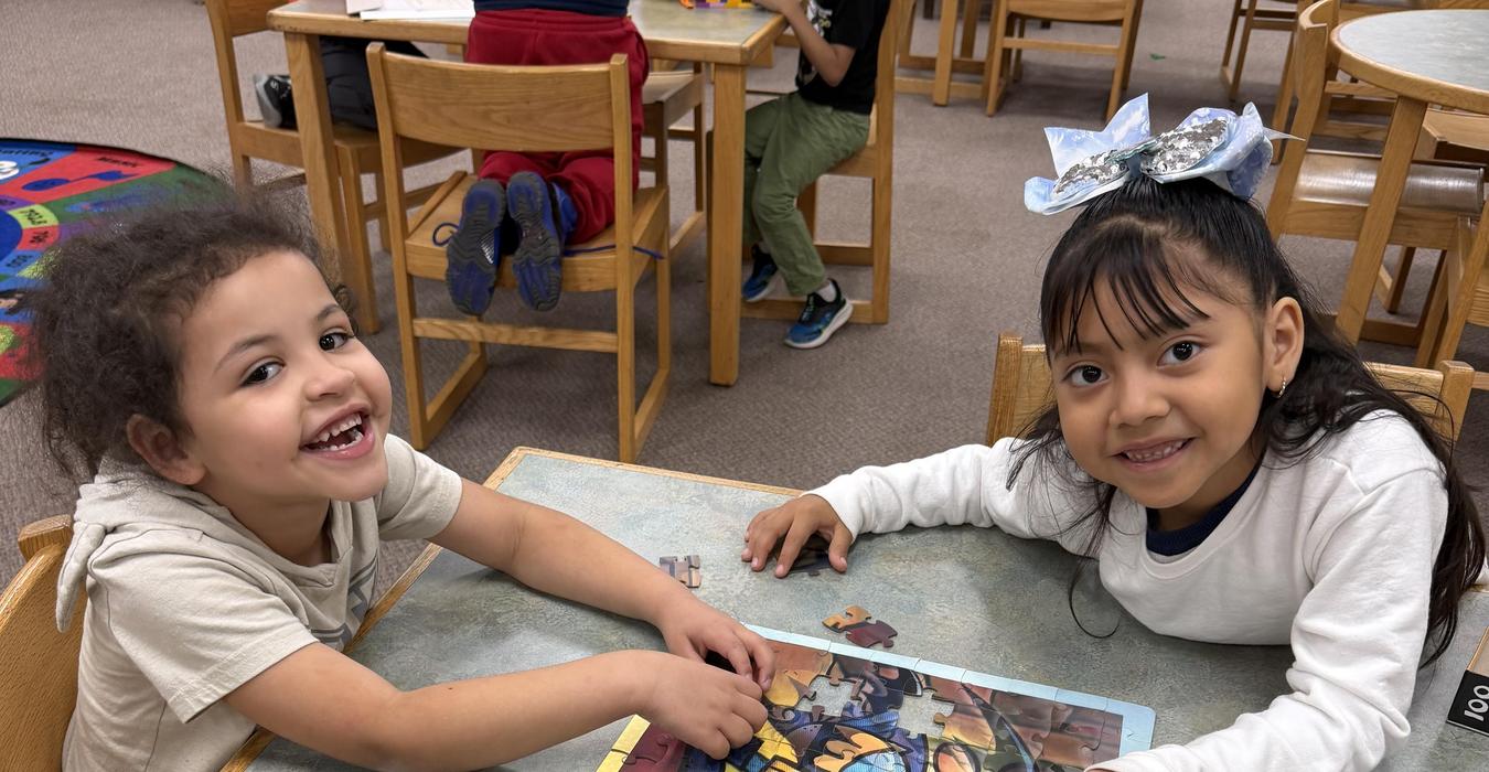 Two smiling children assembling a colorful jigsaw puzzle at a table.