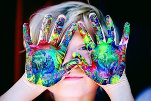 A child holding paint-covered hands in front of their face