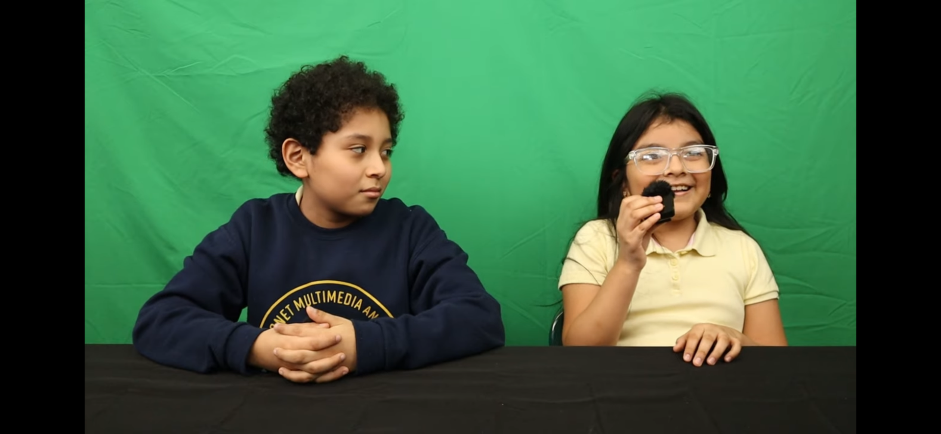 two students in front of a green screen recording a broadcast